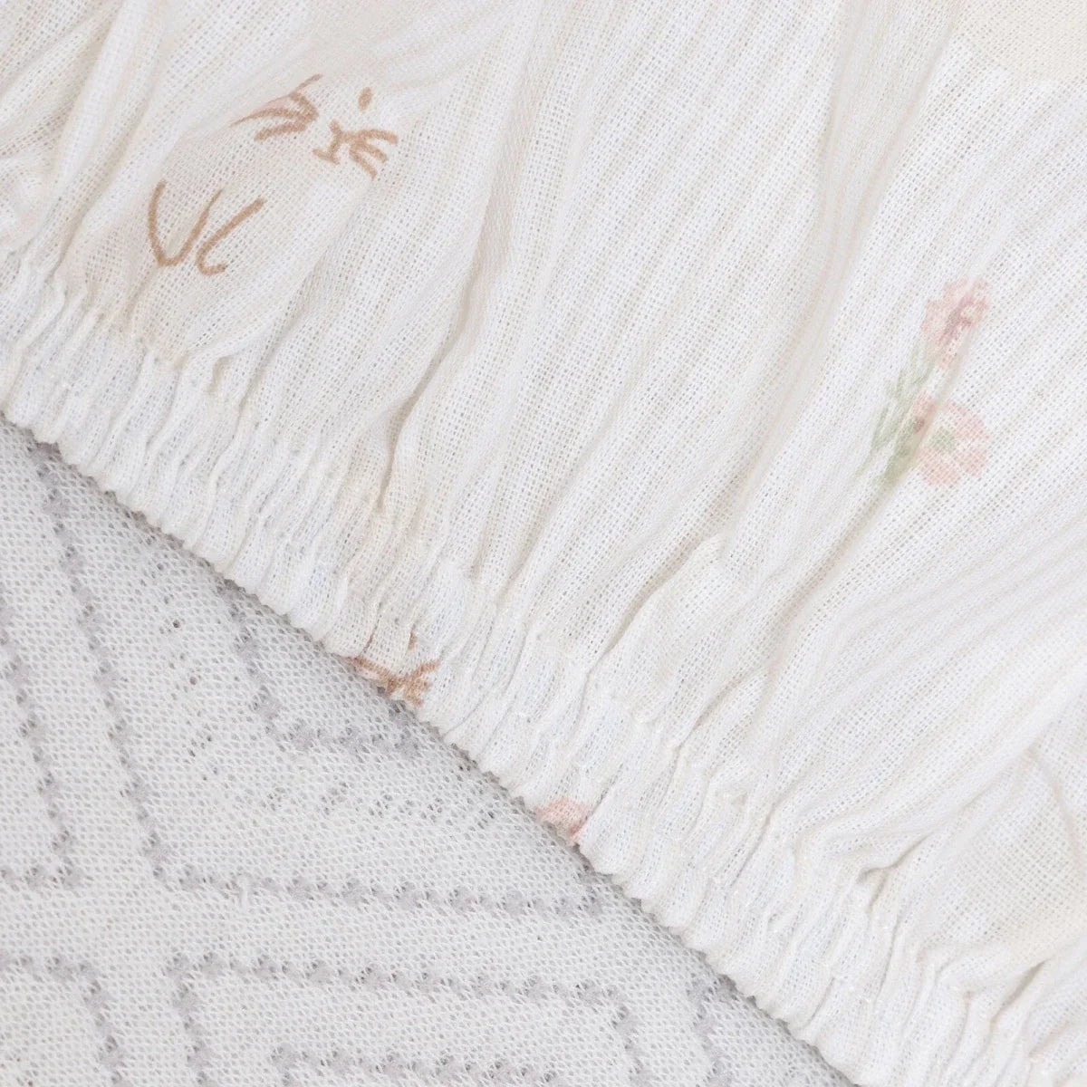 White baby sheet edge with textured stitching and small pastel floral motifs