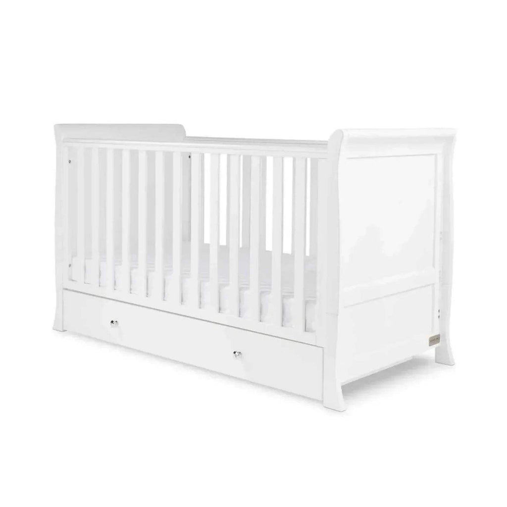 White cot bed with slatted side rails and drawer base, shown at a corner angle.