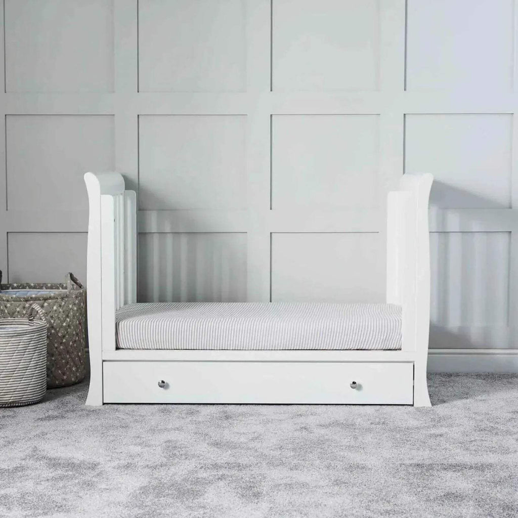 White baby crib with striped mattress and drawer base