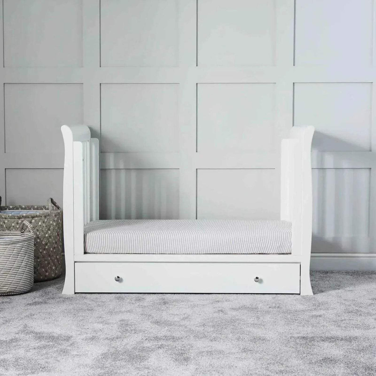 White baby crib with striped mattress and drawer base