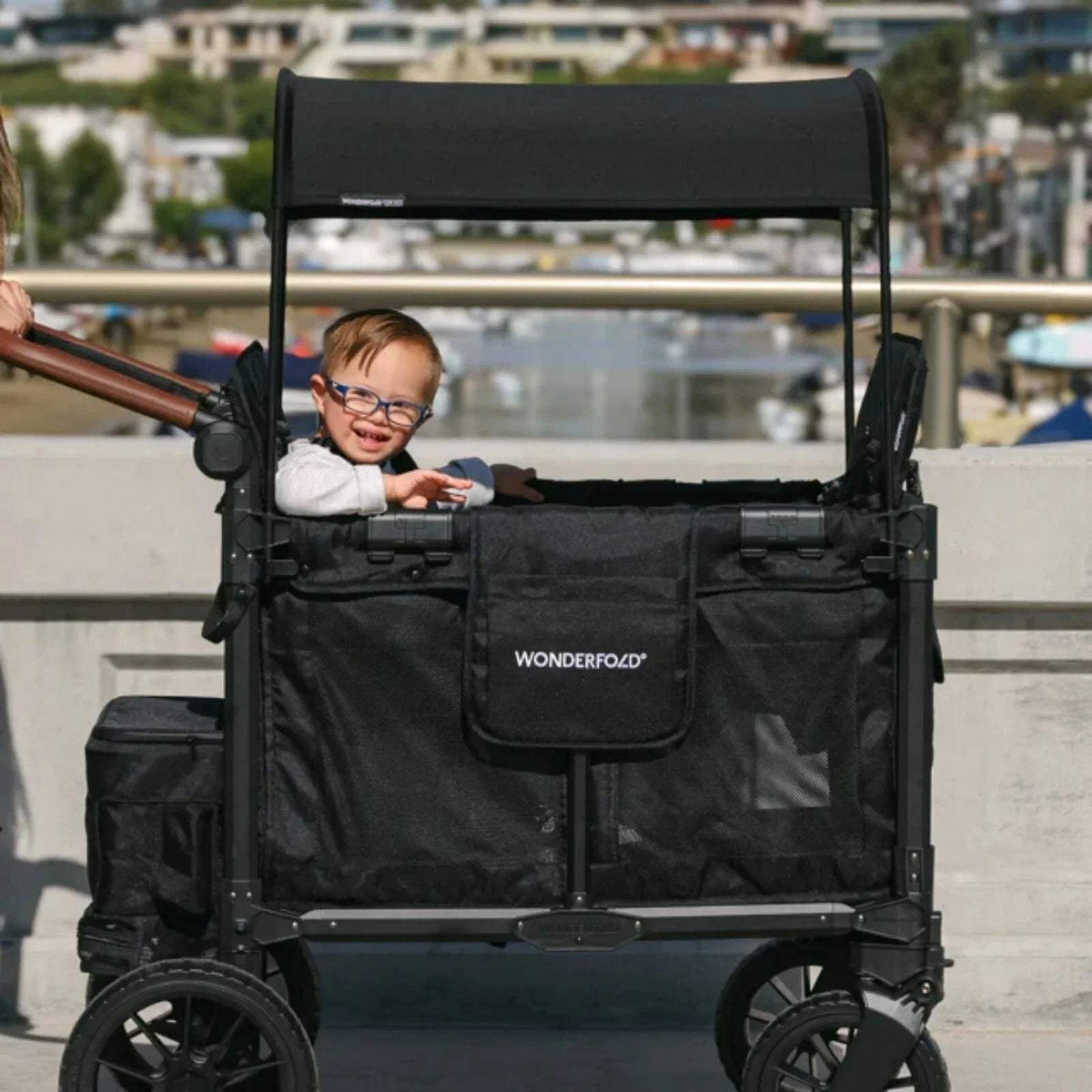 Black stroller wagon with child seated inside, front pocket and canopy