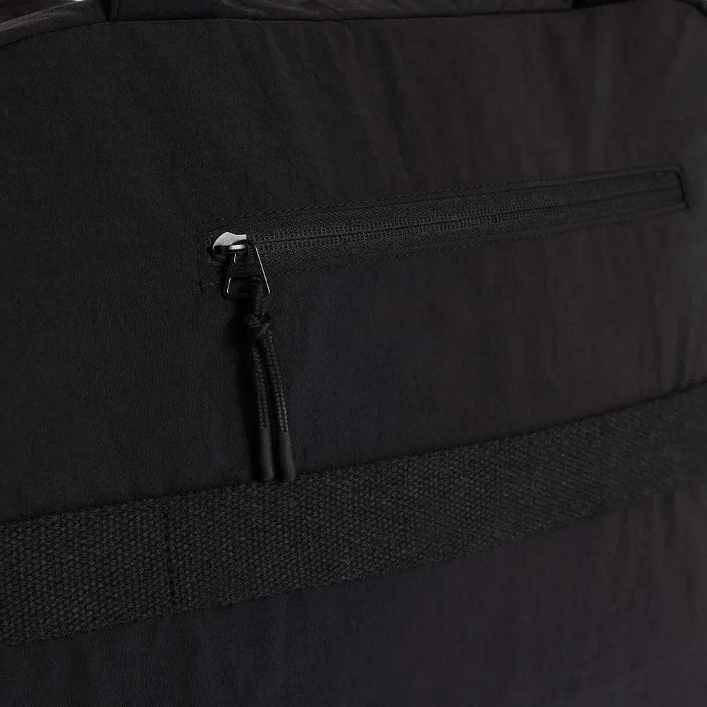 Black quilted shoulder bag close-up of front zipper pocket and metal pull tab