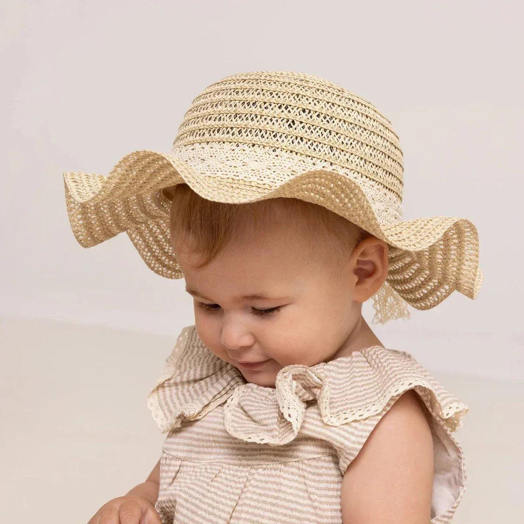 Ecru straw baby hat worn by child, wide brim with ribbon ties