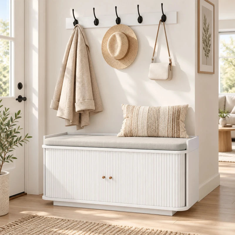 White hallway storage bench with top seat and wall coat hooks over closed cabinet