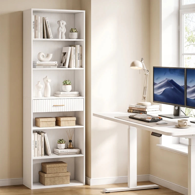 White tall narrow bookshelf with open cubbies and drawer beside a desk