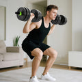 Adjustable dumbbells with black plates and green grips, held during home squat