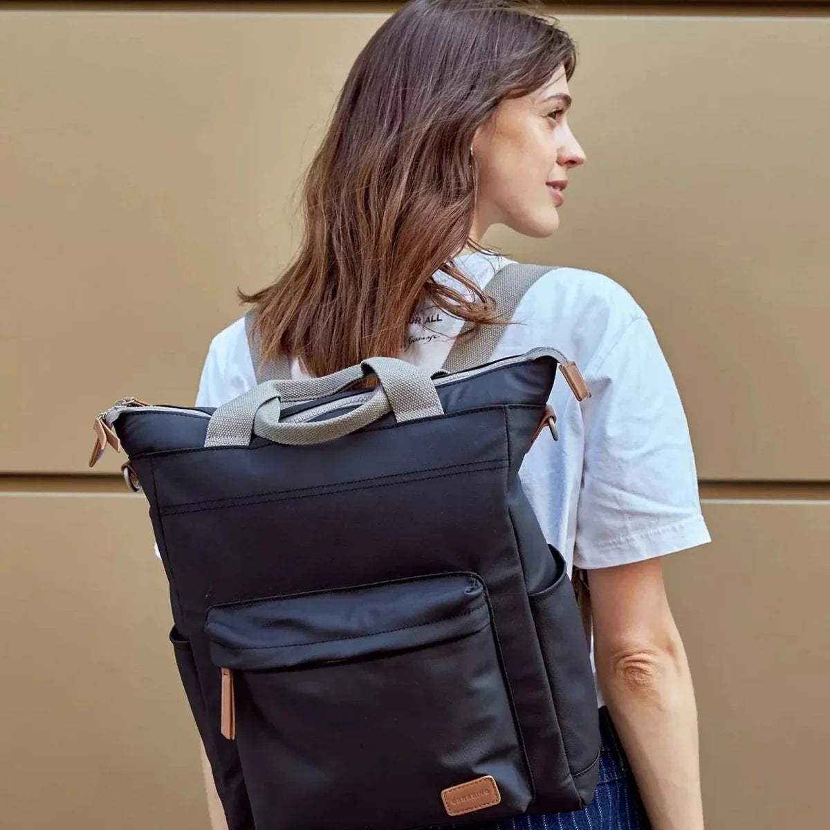 Black changing backpack worn on back with front pocket and tan leather logo patch