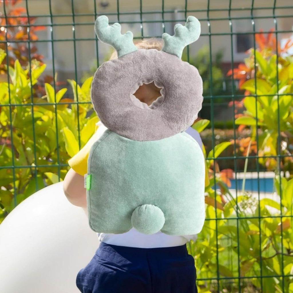 Baby wearing plush gray donut and mint green winged head protector outdoors
