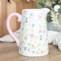 Ceramic flower jug with white body, pink handle, and colorful wildflower pattern