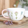 White floral ceramic mug with pastel wildflower stems and pink handle