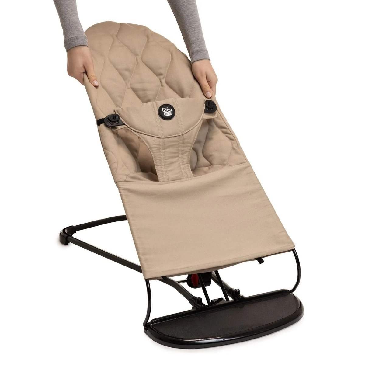 Beige baby bouncer being held upright, black base and padded seat with harness