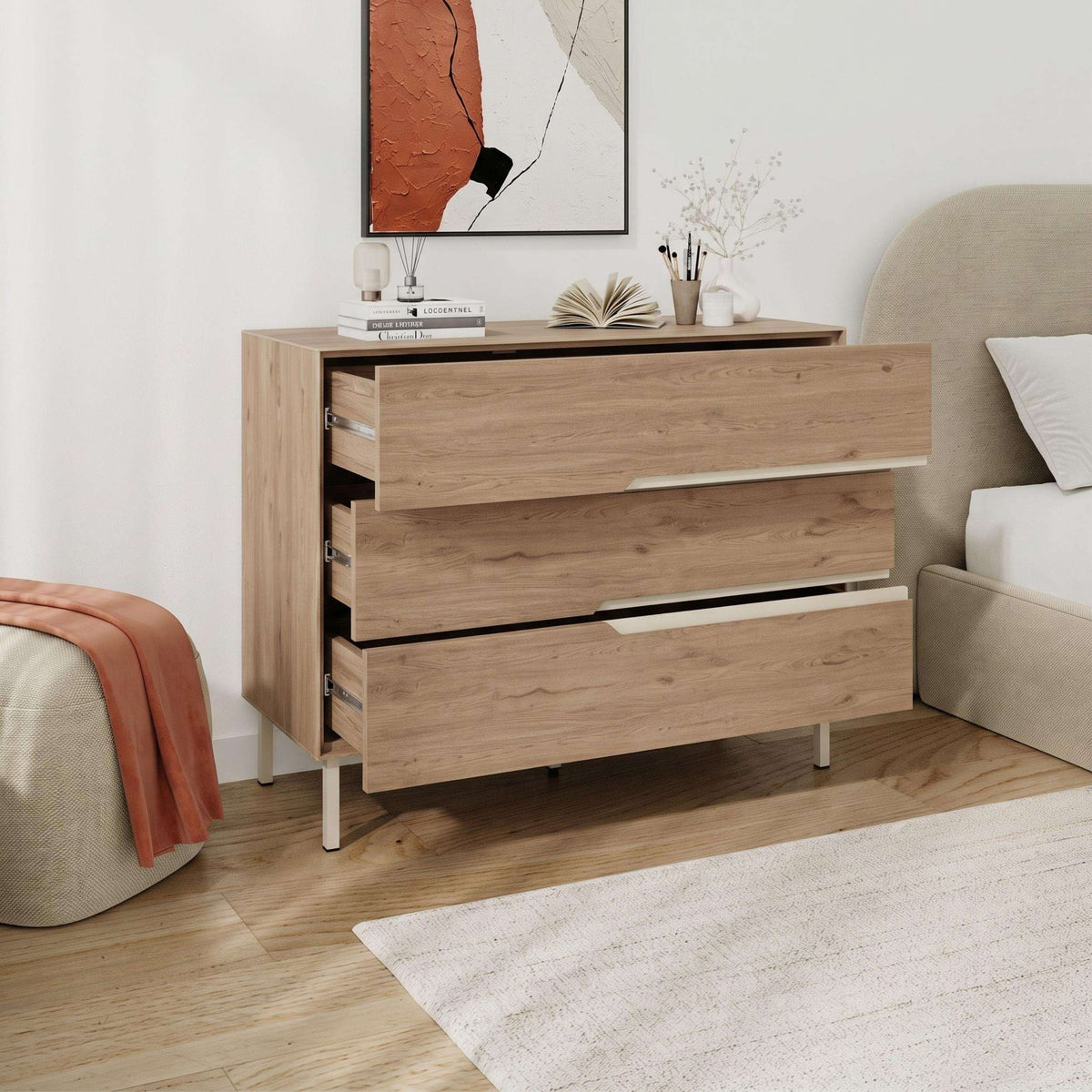Light wood chest of drawers with three drawers and long white handles on slim legs