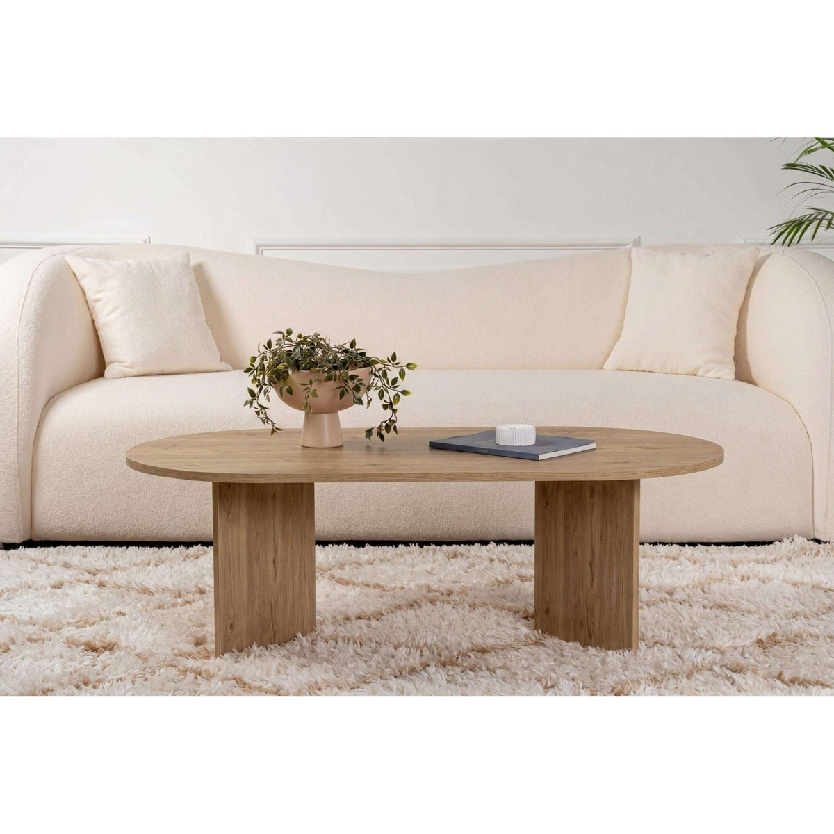 Oak oval coffee table with smooth round top and pedestal-like legs.