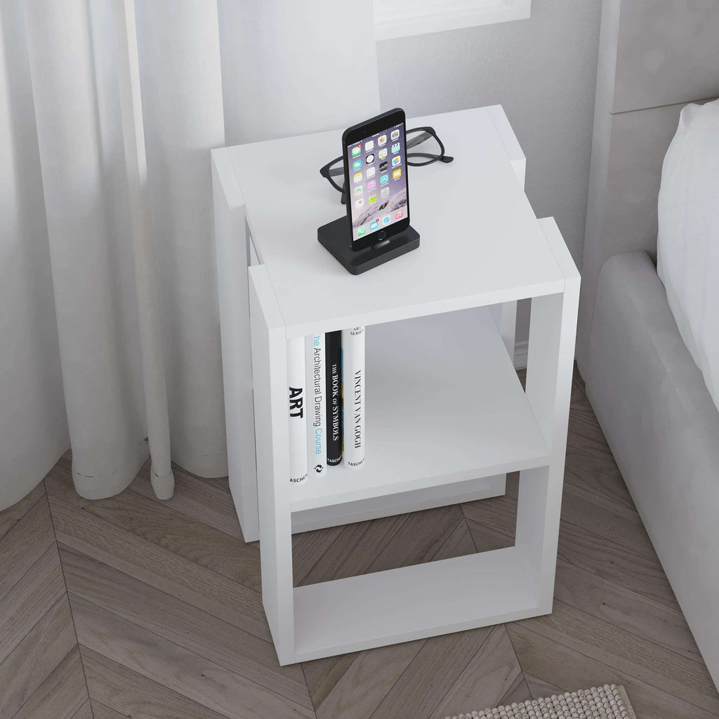 White bedside table with open shelves holding a phone and books