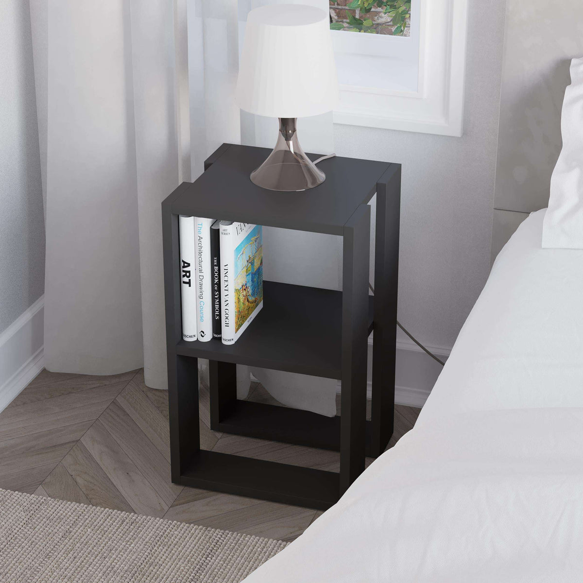 Black bedside table with two open shelves, lamp on top and books inside