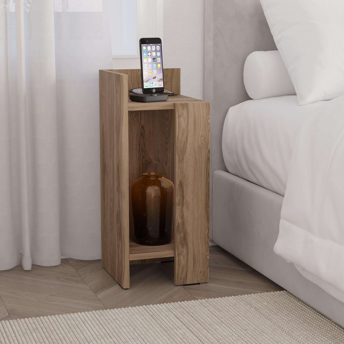 Narrow oak bedside table with open front shelf holding a phone and bottle
