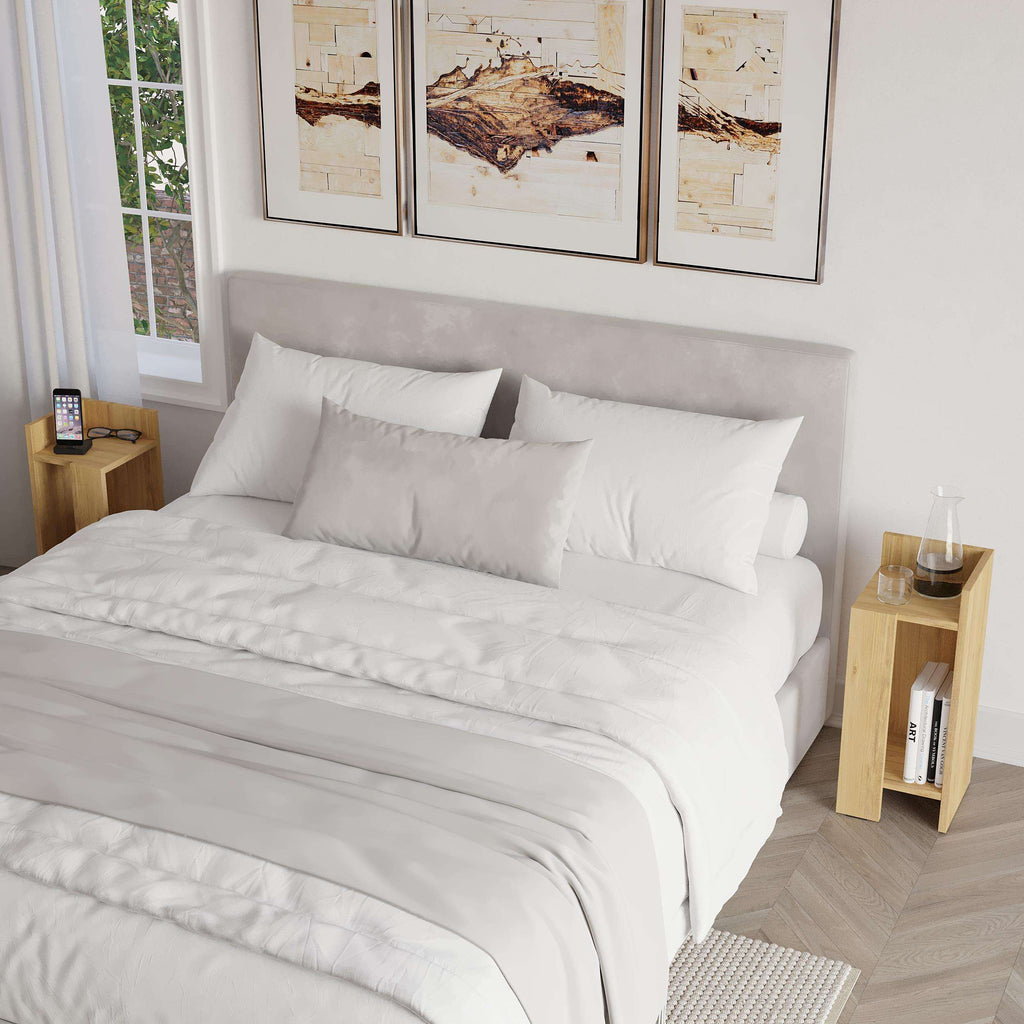 Narrow bedside table with open shelf and light wood finish beside bed