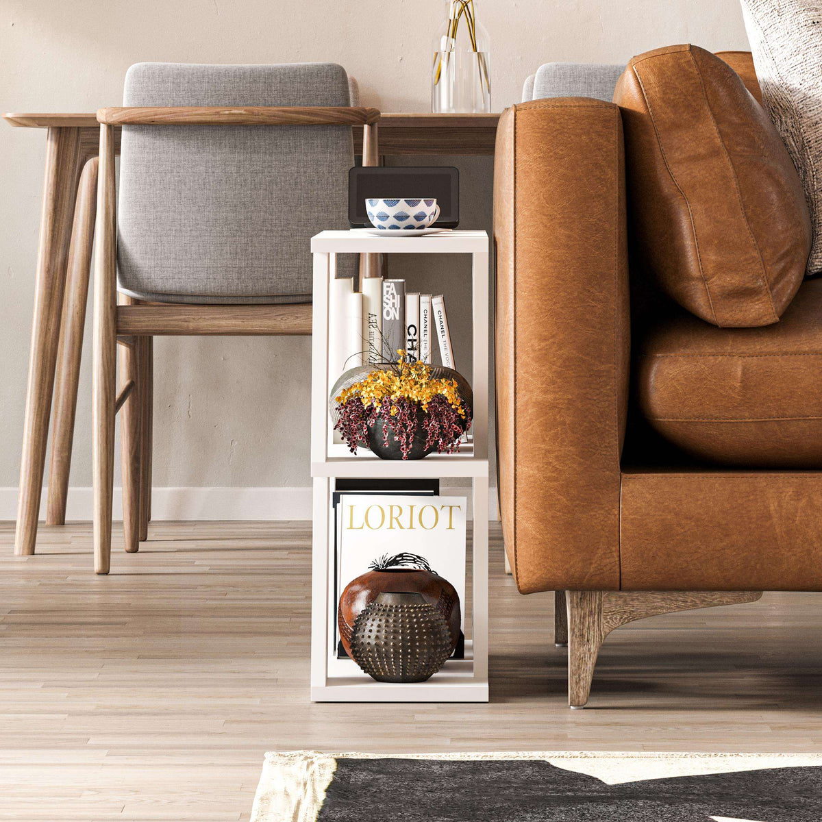 White open-shelf side table with tabletop cup and books, beside brown leather sofa