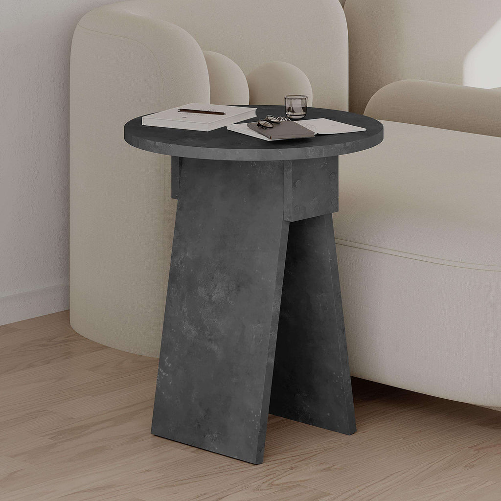 Dark grey round side table with stone-look finish and angular pedestal legs