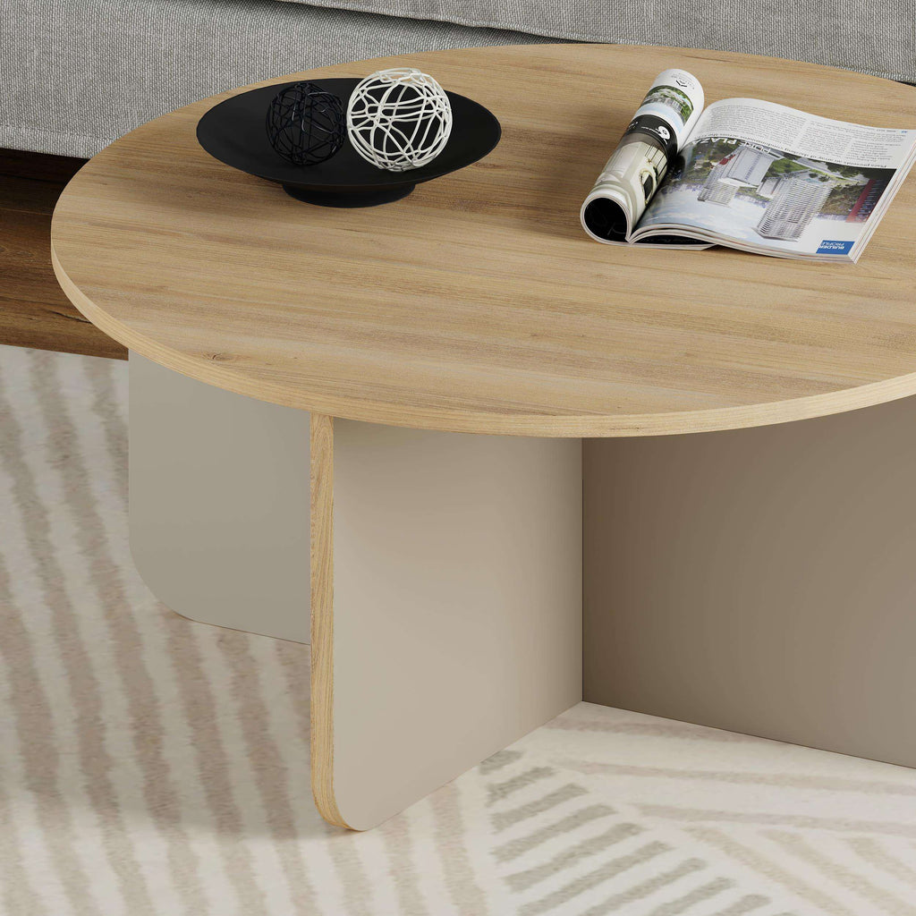 Round coffee table close-up with light wood top and magazines and decor on surface.