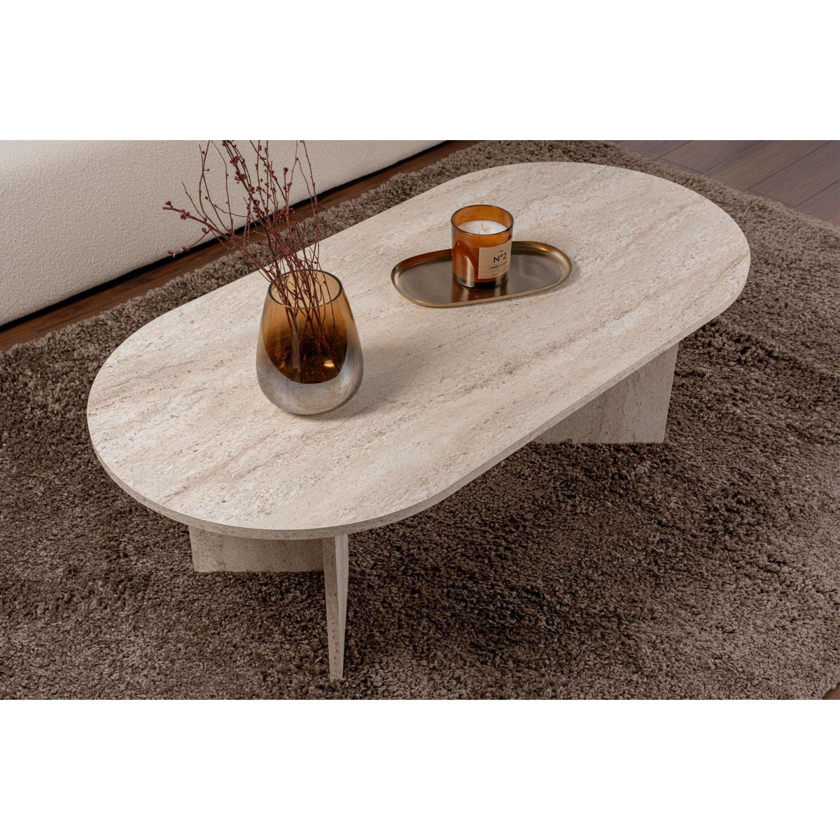 Oval stone coffee table with slender legs, light travertine-style top and rounded edges