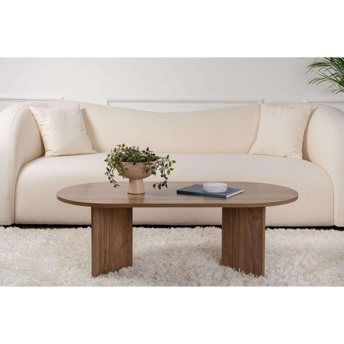 Oval walnut coffee table with rounded top and two-part legs on a rug