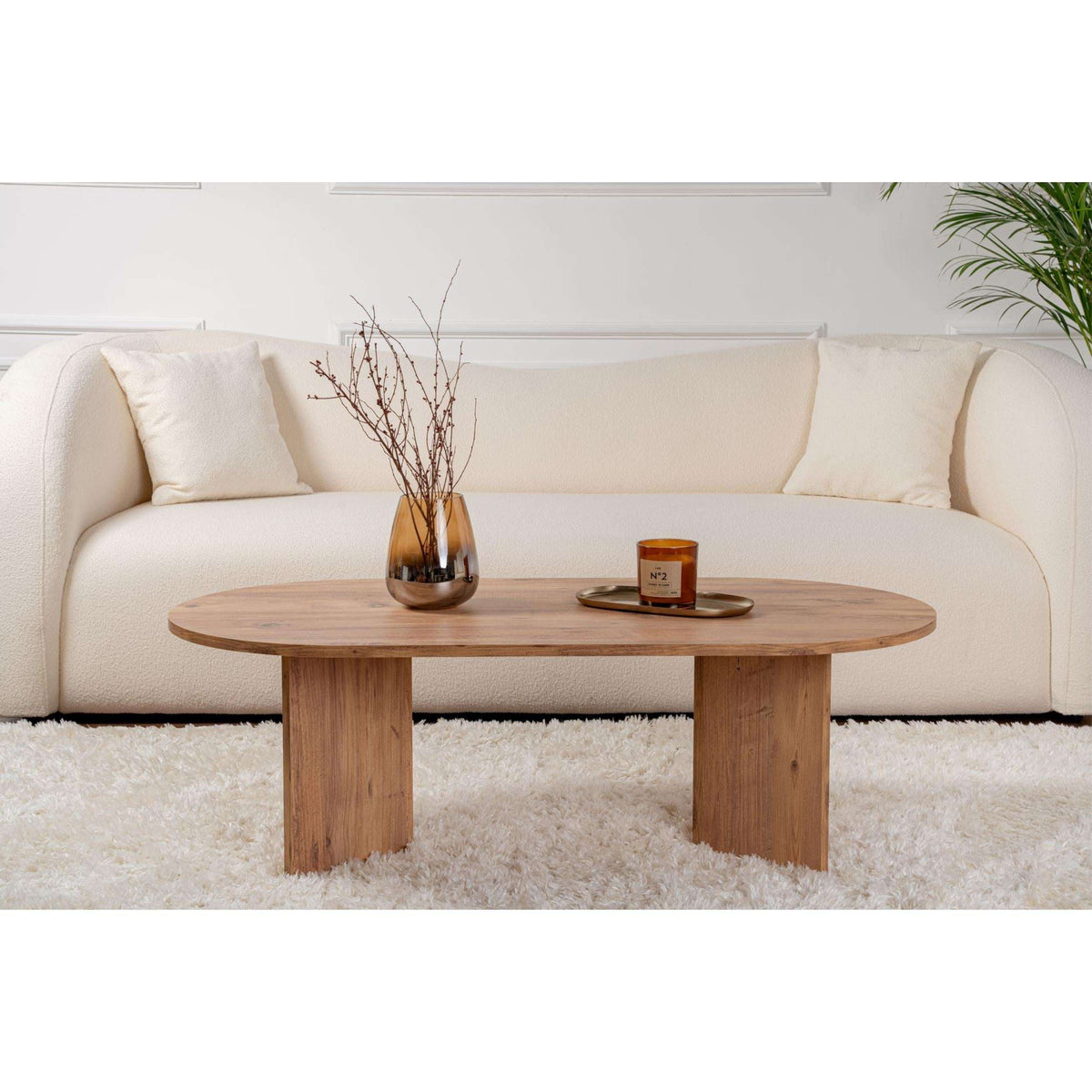Natural wood oval coffee table with tapered legs in front of a sofa.