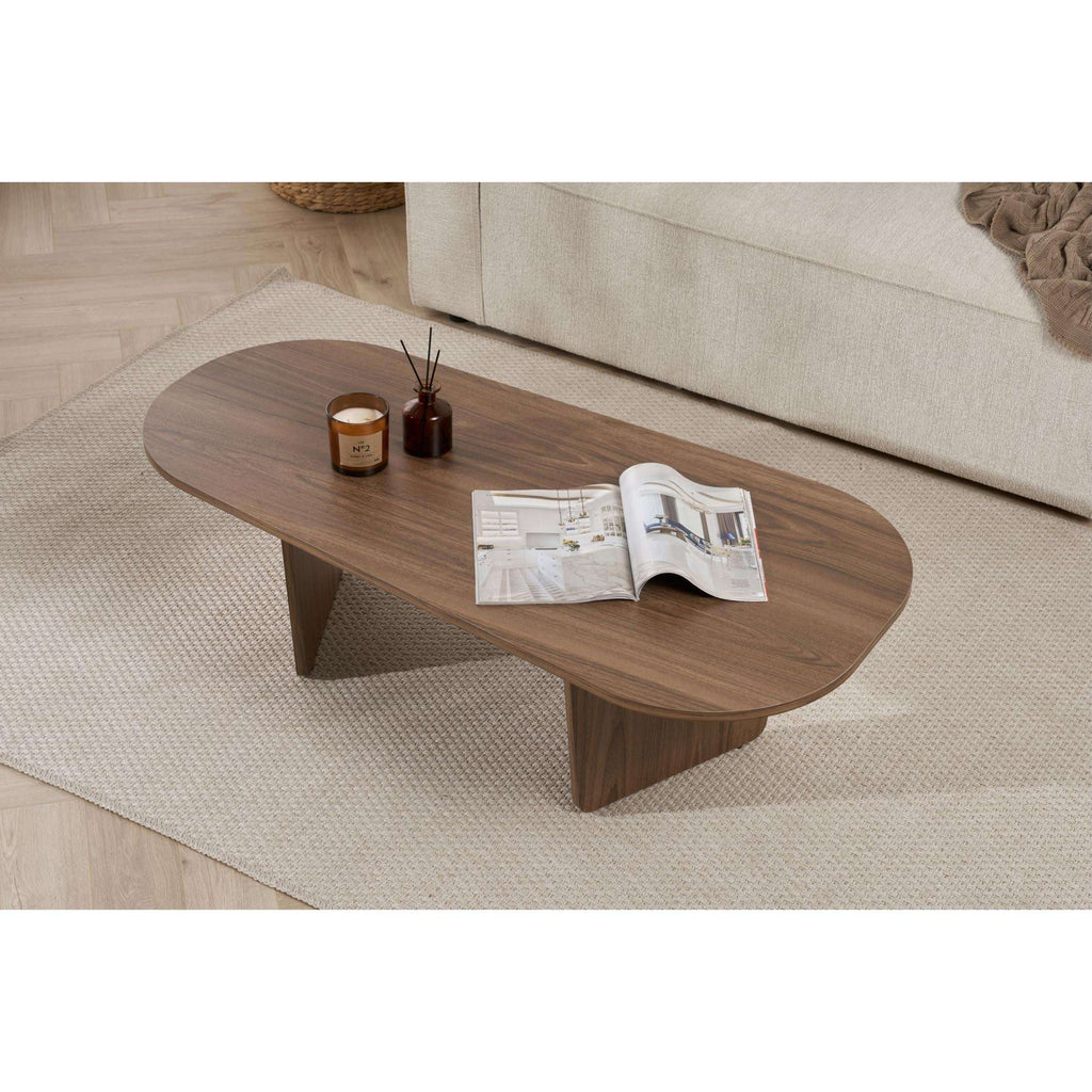 Oval coffee table in walnut-toned wood, tapered legs, magazine and candles on top
