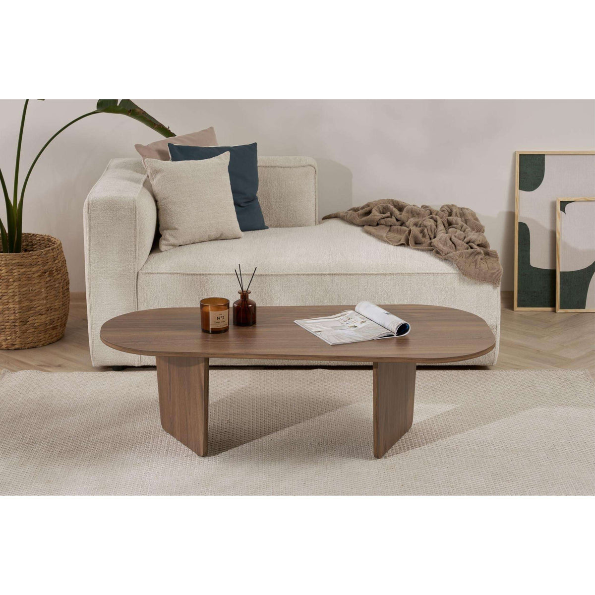 Oval coffee table in walnut-toned wood with rounded edge, decor and magazine on top