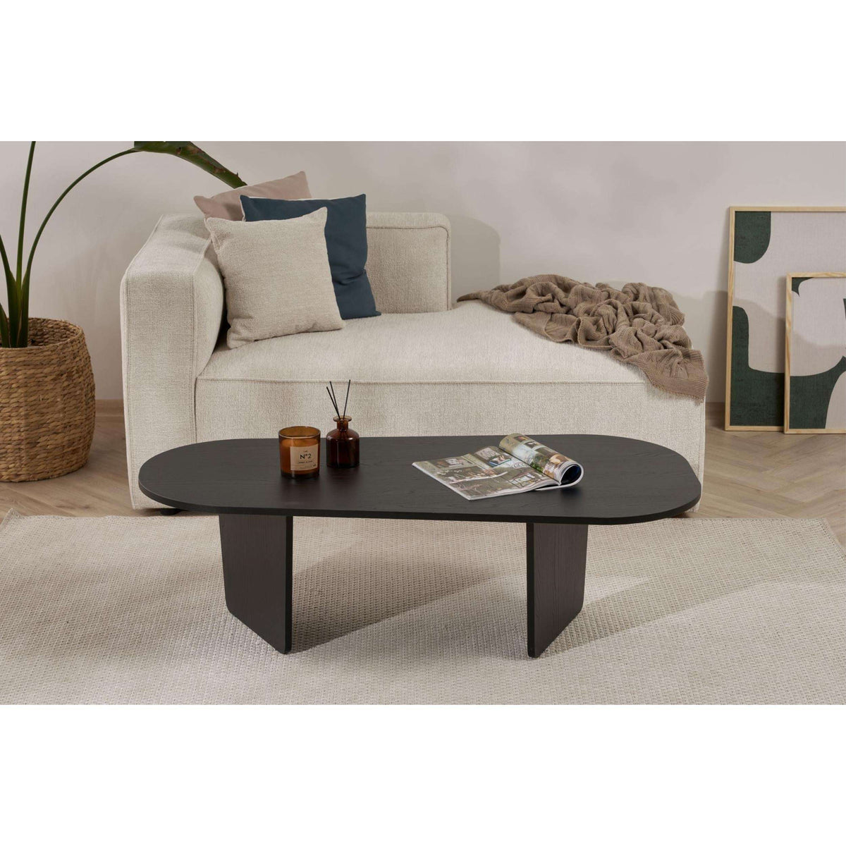 Dark oval coffee table with rounded top, sculpted base, and tapered legs