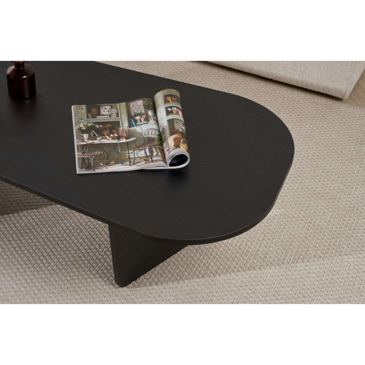 Dark oval coffee table with chamfered edges and central sculpted legs