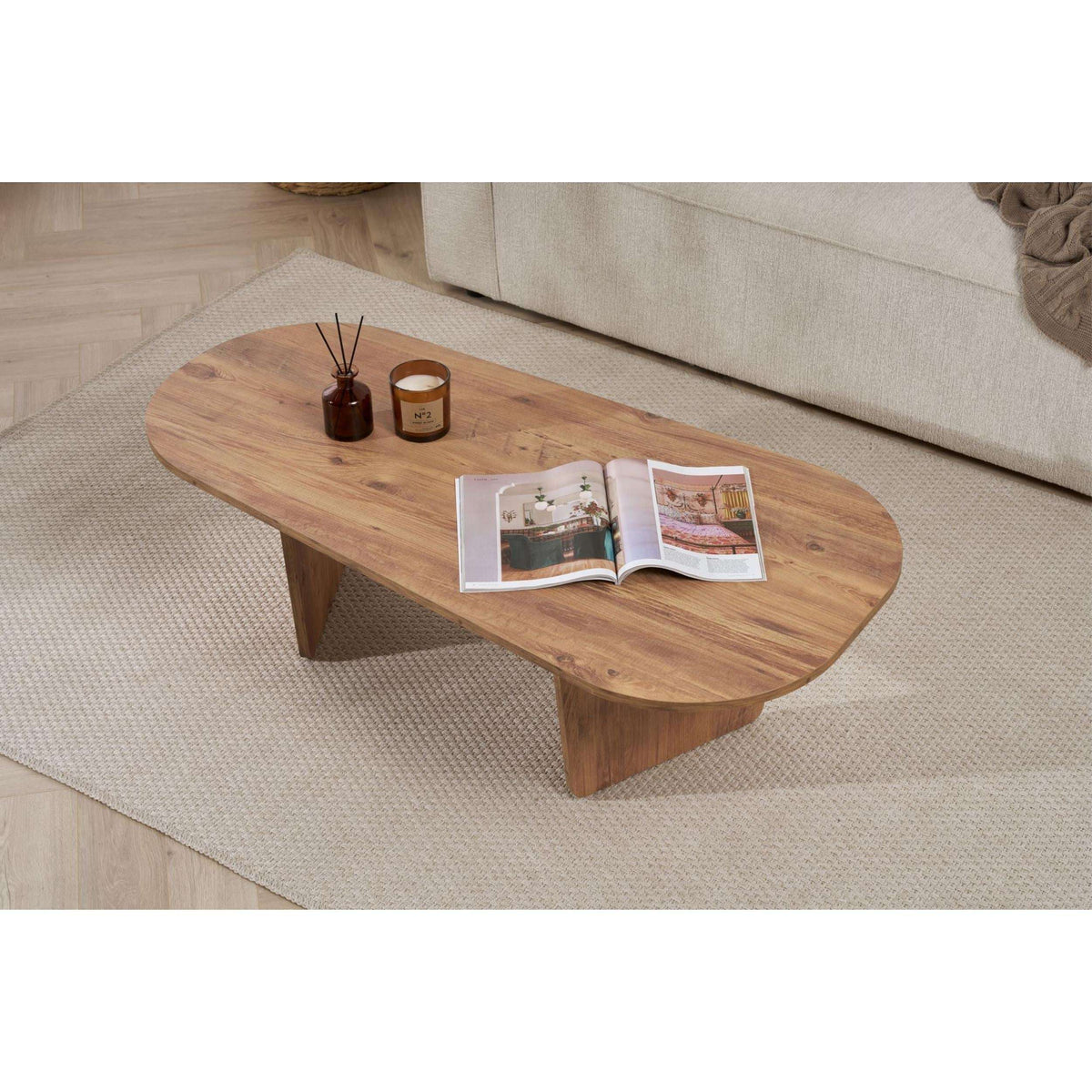 Natural wood oval coffee table with angled legs and a magazine on top