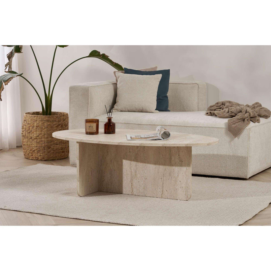 Oval light stone coffee table with candles and an open magazine on top.