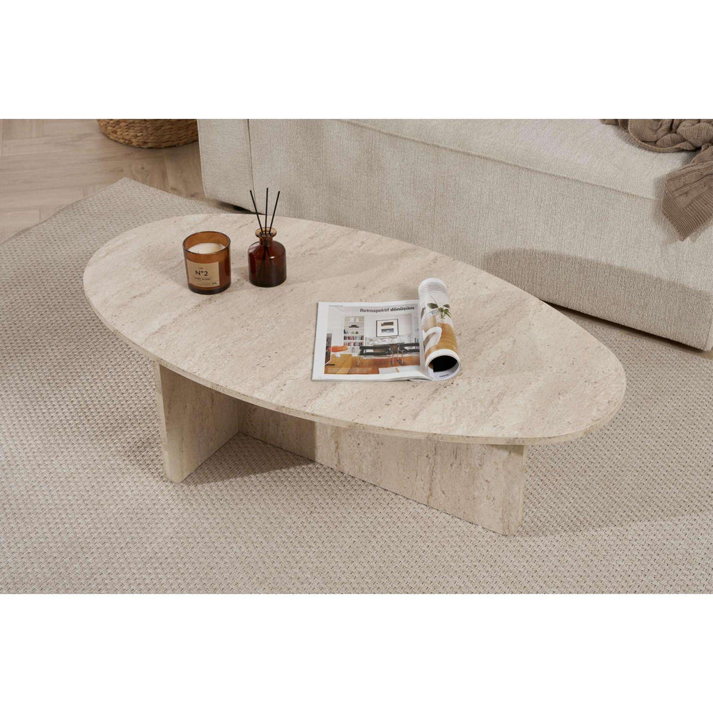 Oval light stone coffee table with rounded edge, candles, and open magazine.