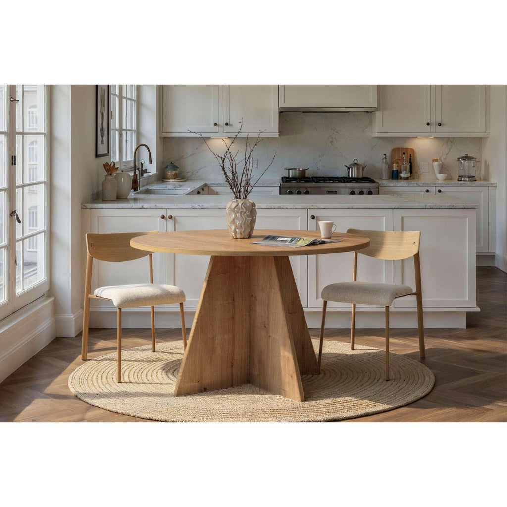 Round light-wood dining table with tapered pedestal base and dining chairs