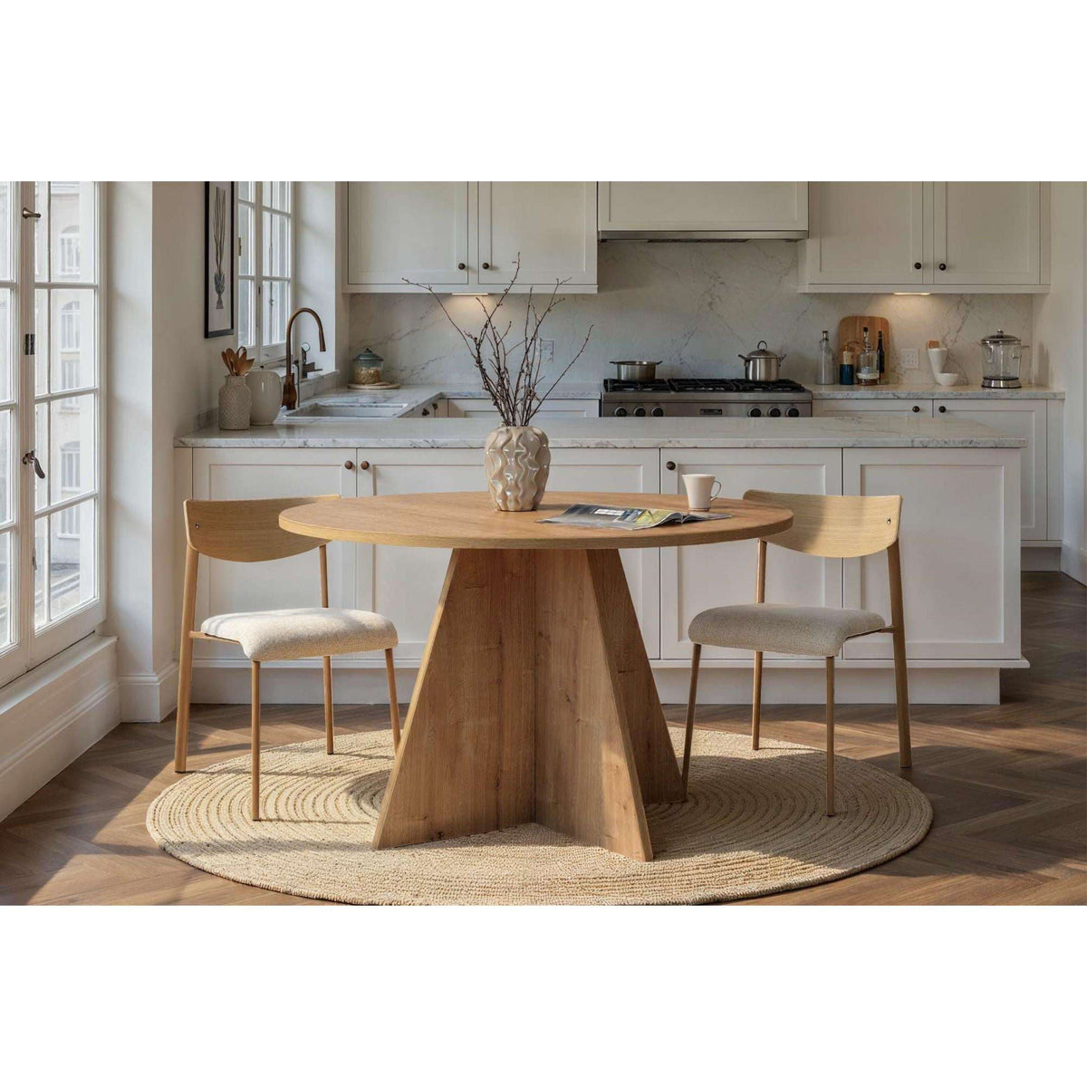 Round light-wood dining table with tapered pedestal base and dining chairs