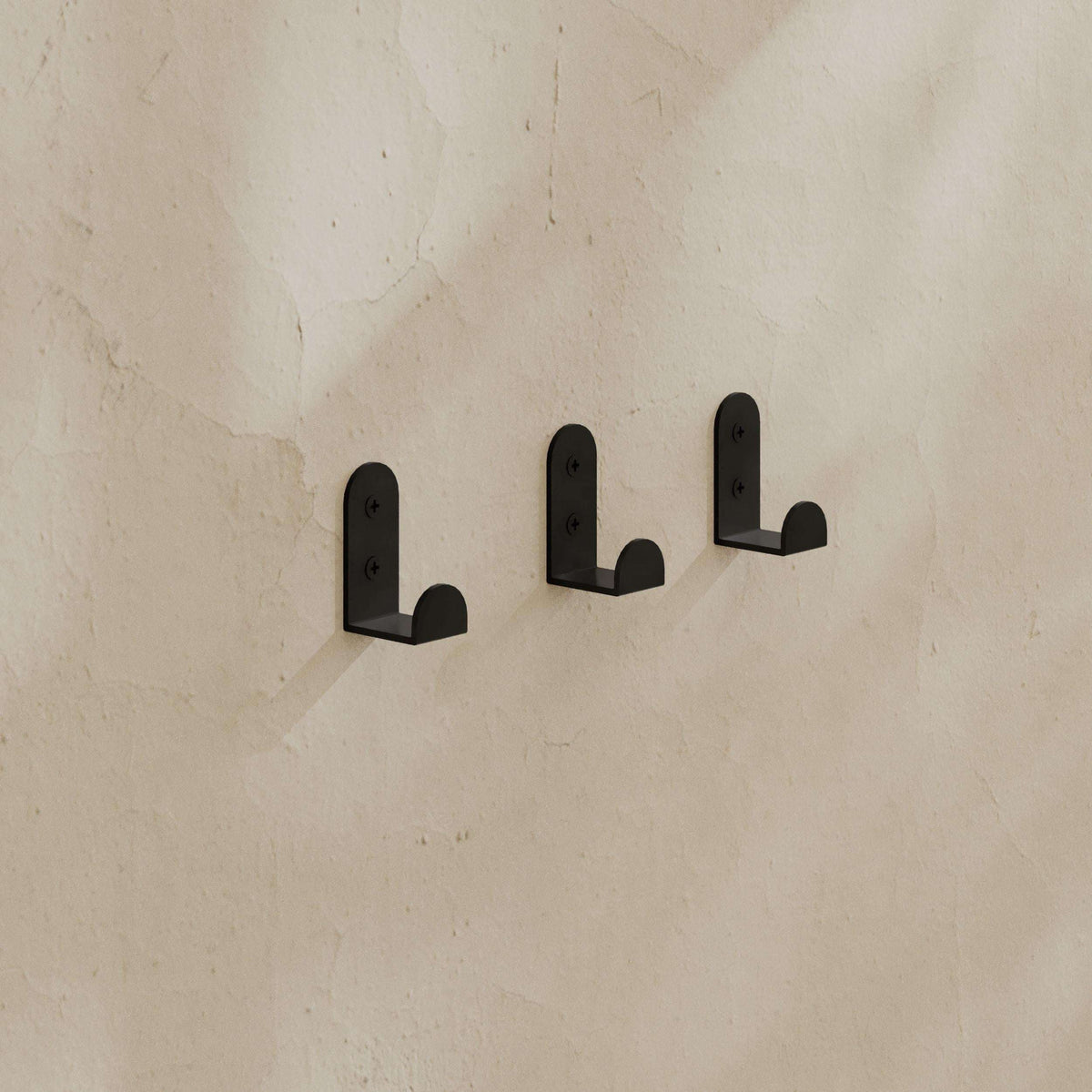 Set of 3 black metal wall coat hooks mounted on a wall