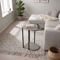 C-shaped side table with round top, lower shelf, and black legs in light gray finish