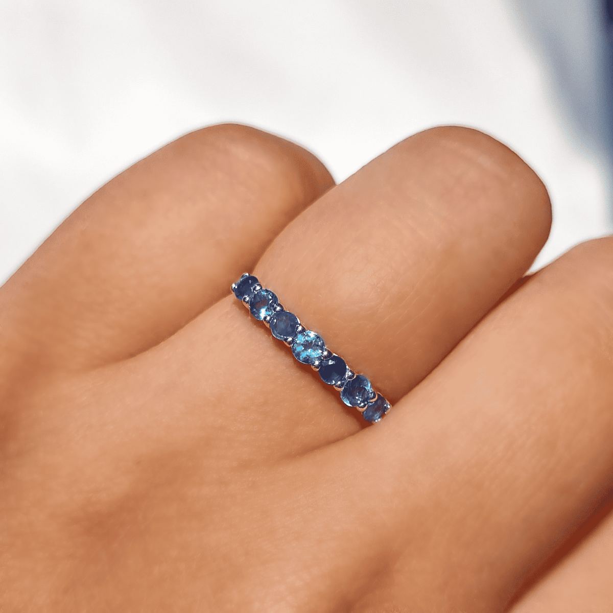 Half-eternity band in sterling silver with oval blue gemstones on finger