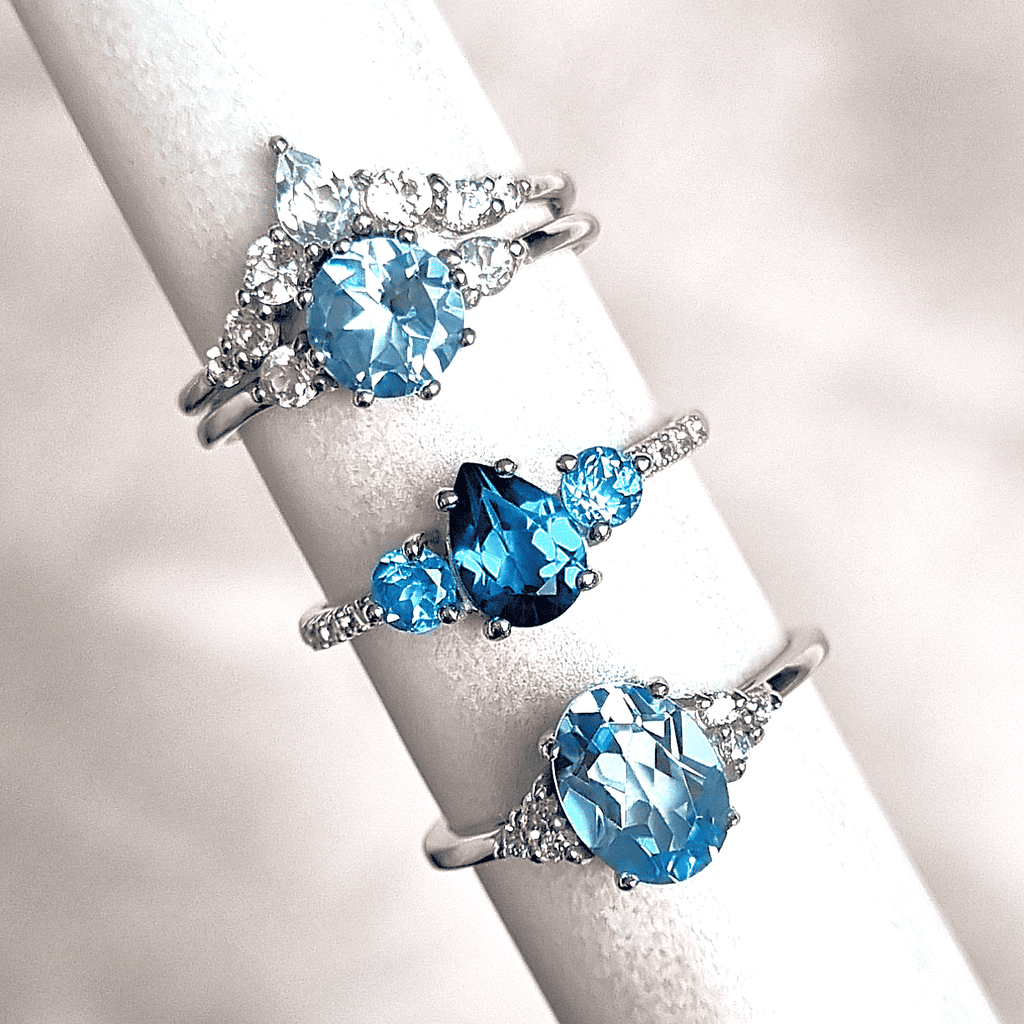 Three sterling silver rings with oval blue topaz centers and clear stone halos