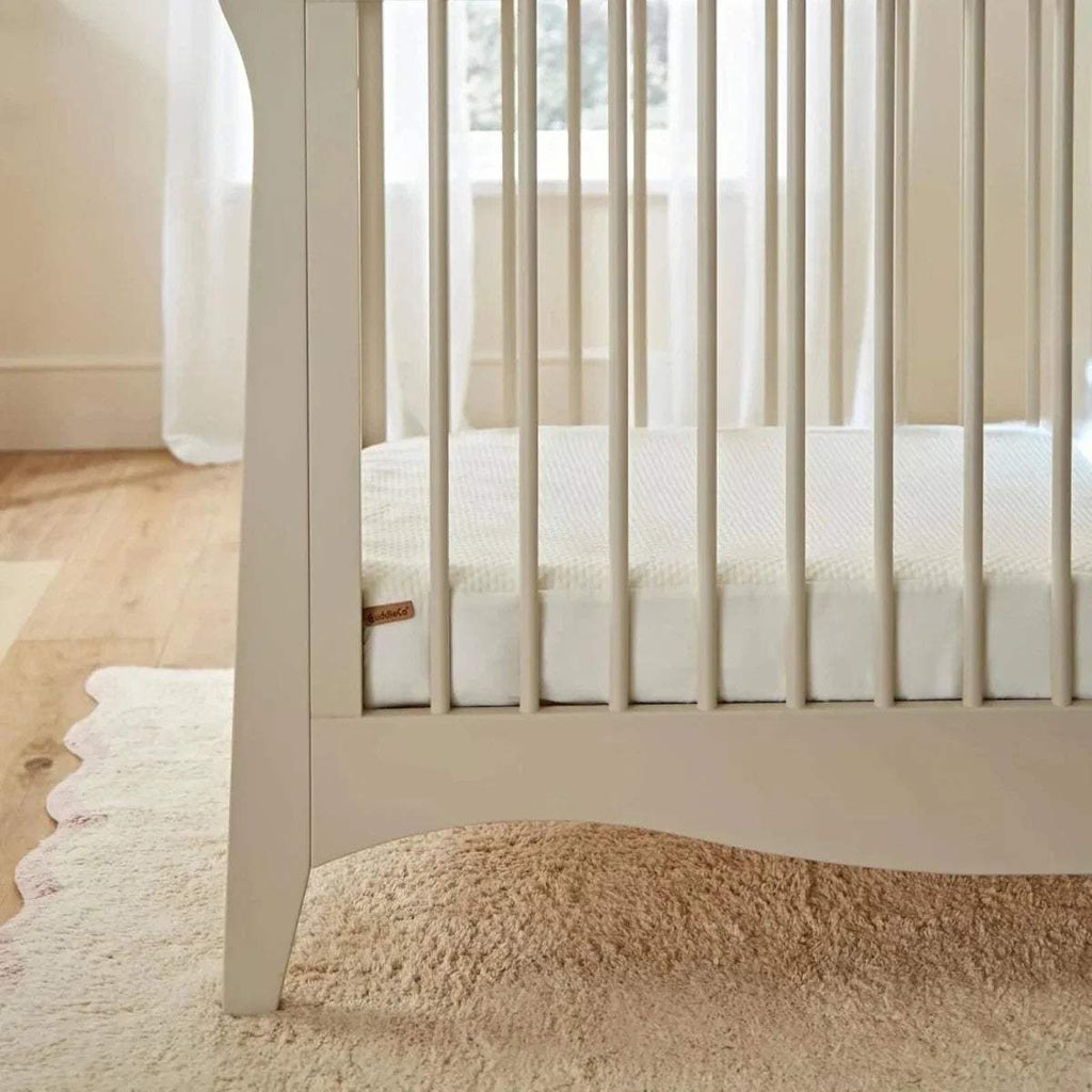 Cot bed mattress protector fitted on slatted cot, white quilted waterproof cover.
