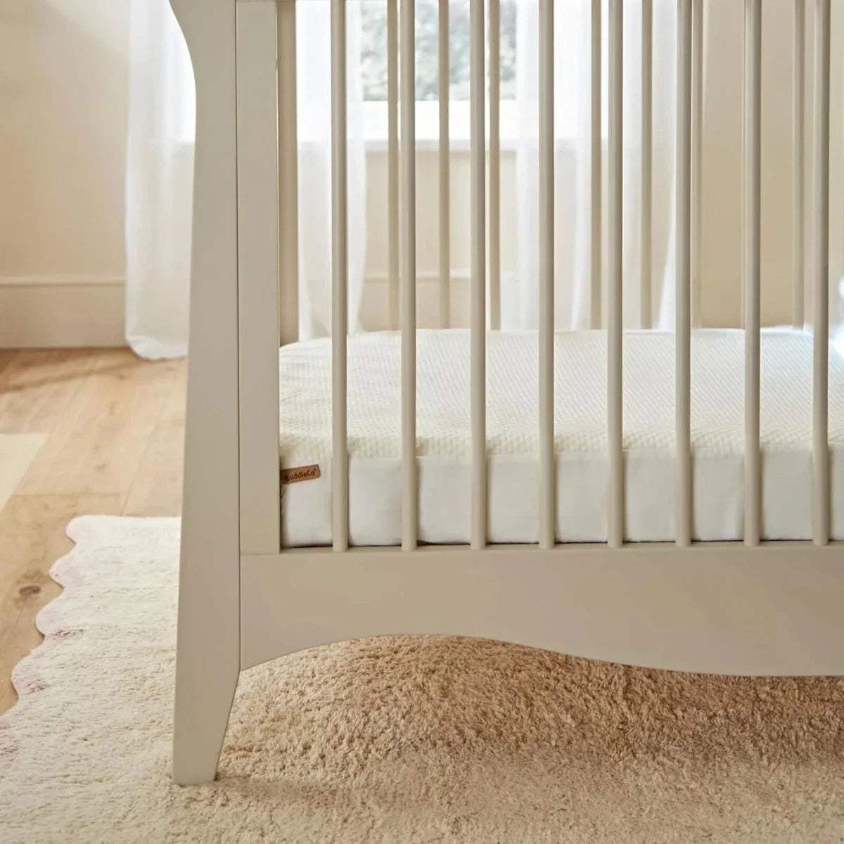 Cot bed mattress protector fitted on slatted cot, white quilted waterproof cover.