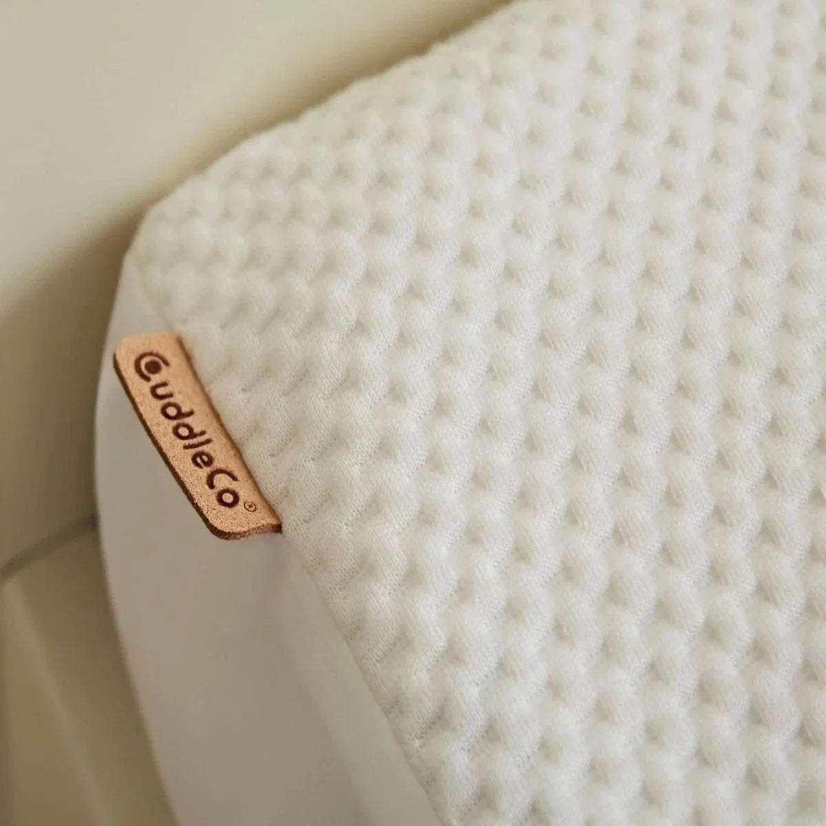 White waterproof mattress protector corner tag with CuddleCo branding, textured knit fabric.