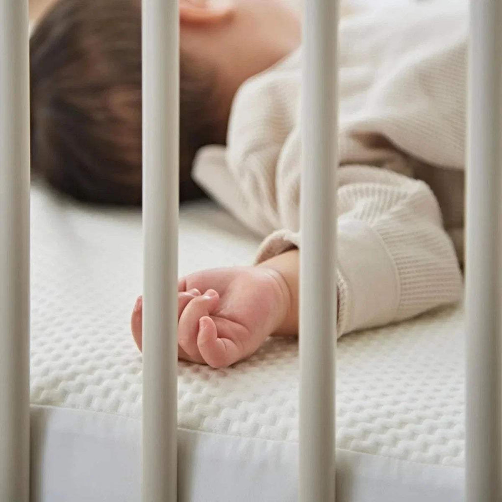 Baby feet resting on white waterproof cot bed mattress protector with textured surface.