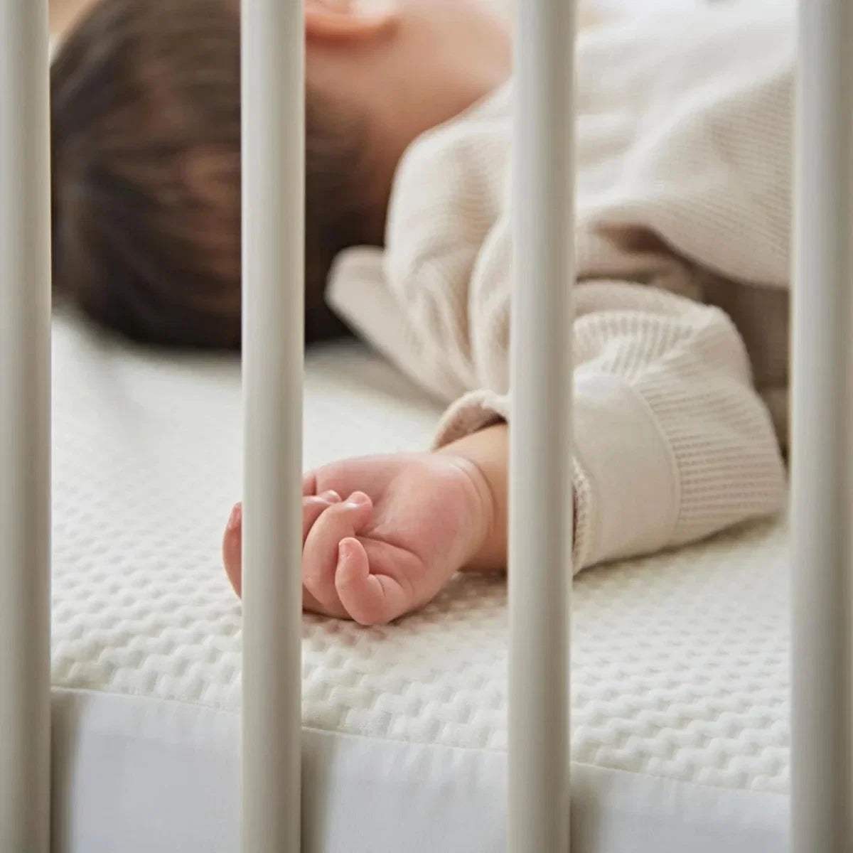 Baby feet resting on white waterproof cot bed mattress protector with textured surface.