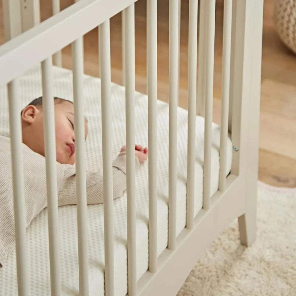 Baby sleeping on white waterproof cot bed mattress protector fitted on crib mattress.