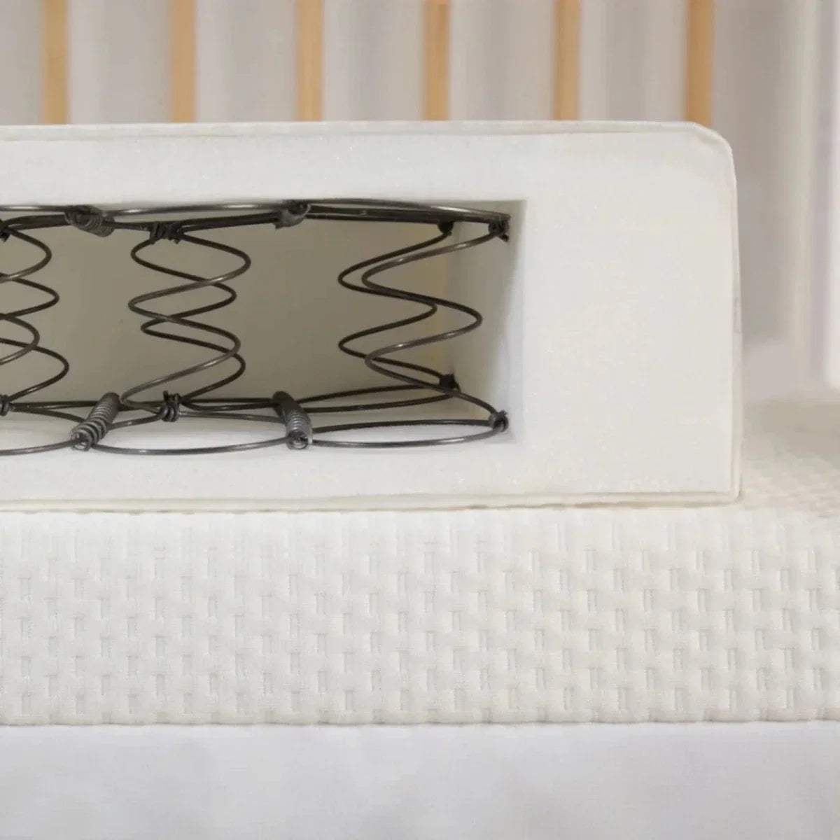 Cot bed mattress with visible pocket springs in a white cover, side close-up.