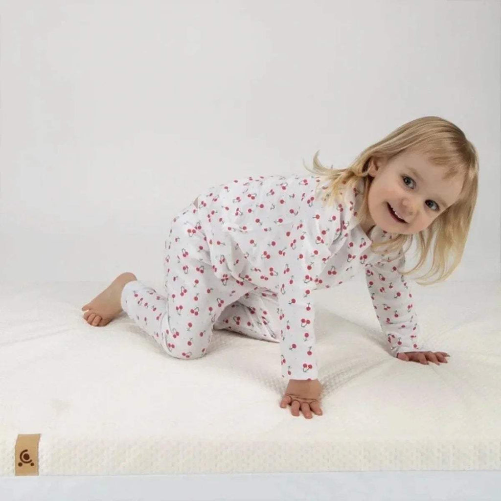 Cot bed mattress with white cover, child lying on top on soft surface.