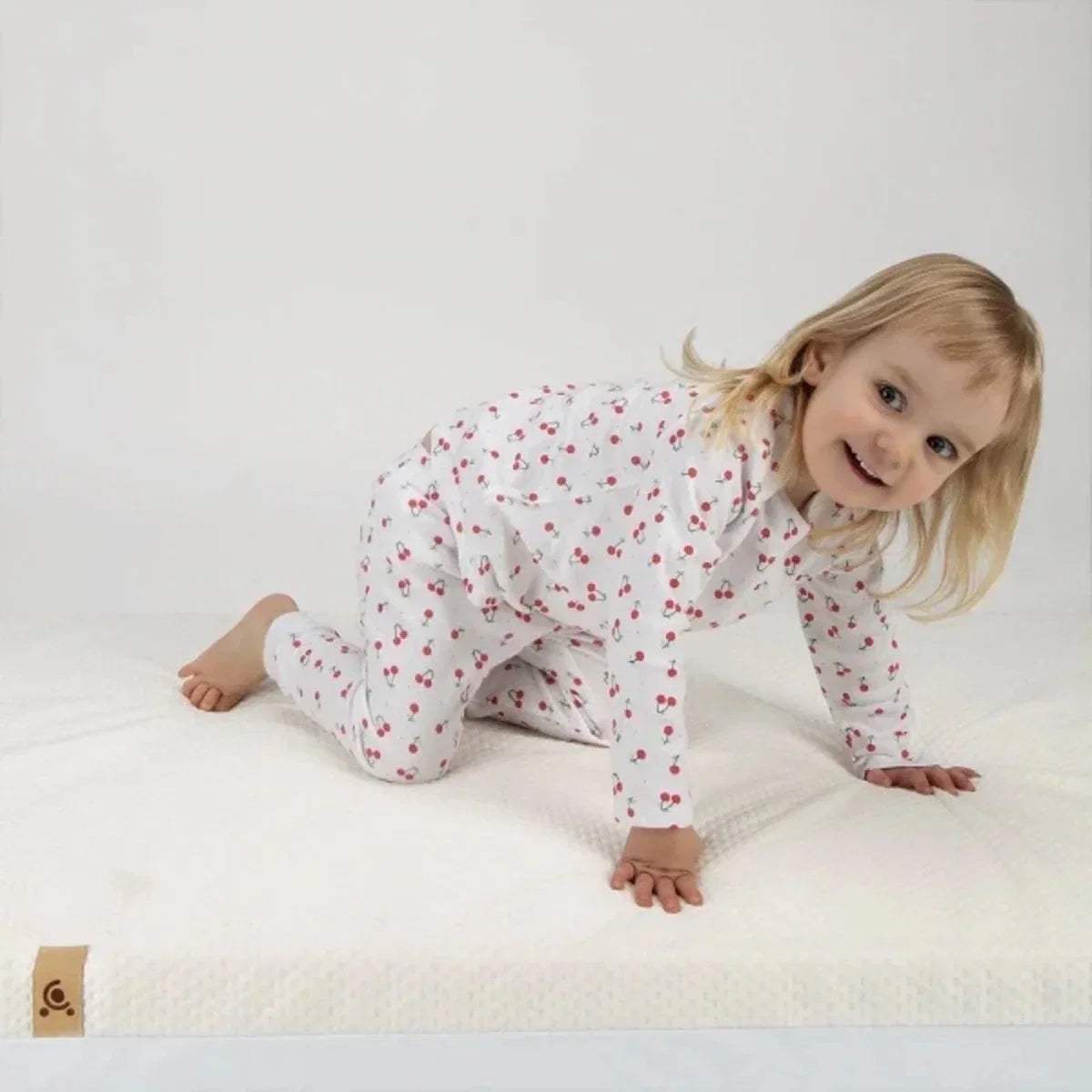 Cot bed mattress with white cover, child lying on top on soft surface.