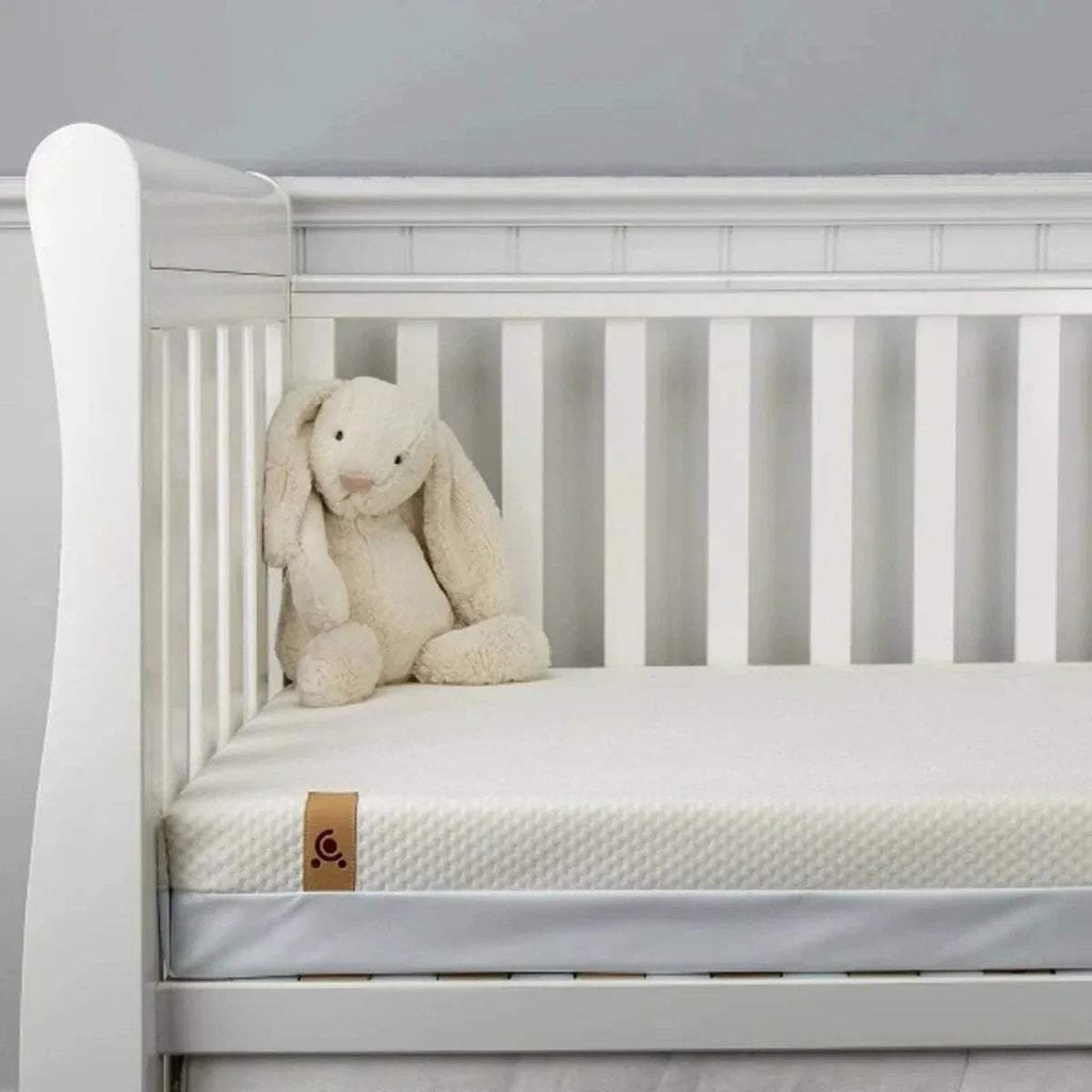 White cot mattress with coil springs shown on a slatted bed, with teddy bear